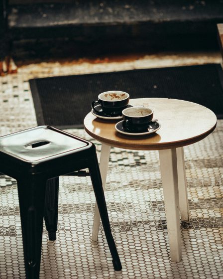 zdjęcie stolika w stylu retro na którym są dwie filiżanki kawy i obok taburet