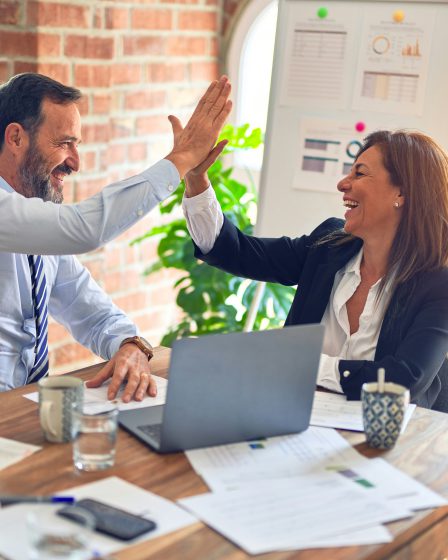 Dwie osoby siedzą przy biurku w jasnym pomieszczeniu i przybijają sobie piątkę
