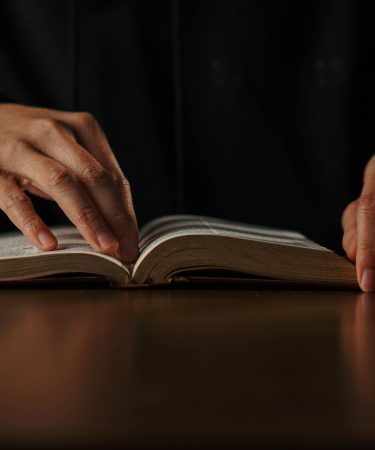 Dłonie osoby spoczywają na otwartej książce leżącej na stole