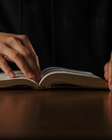 Dłonie osoby spoczywają na otwartej książce leżącej na stole