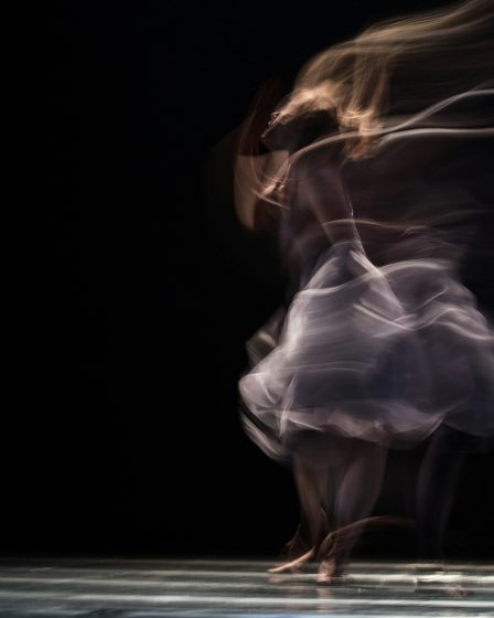 Na zdjęciu widać tancerkę uchwyconą w ruchu na ciemnej scenie.