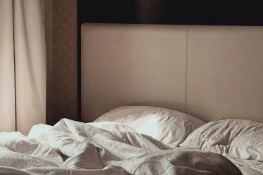 zdjęcie ukazuje niepościelone łóżko w przytulnej, stonowanej sypialni.