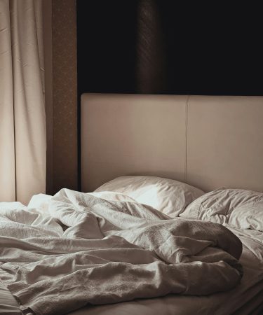 zdjęcie ukazuje niepościelone łóżko w przytulnej, stonowanej sypialni.