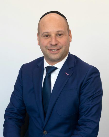 zdjęcie to portret mężczyzny w eleganckim, granatowym garniturze, białej koszuli i ciemnym krawacie