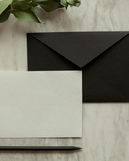 Elegancka czarna koperta i biała karta na marmurowym blacie, prezentujące nowoczesne czarne zaproszenia ślubne w stylu minimalistycznym.