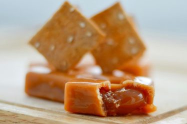 Mleczne krówki z własnym nadrukiem ułożone na drewnianym blacie, z widocznym płynnym nadzieniem karmelowym