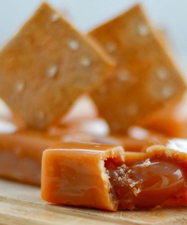 Mleczne krówki z własnym nadrukiem ułożone na drewnianym blacie, z widocznym płynnym nadzieniem karmelowym