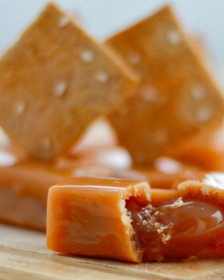 Mleczne krówki z własnym nadrukiem ułożone na drewnianym blacie, z widocznym płynnym nadzieniem karmelowym