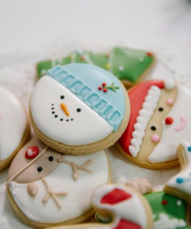 Kolorowe słodycze bożonarodzeniowe w formie okrągłych kruchych ciasteczek dekorowanych lukrem z postaciami Świętego Mikołaja i bałwana.