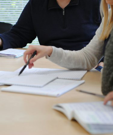 Na zdjęciu przedstawiono dwie osoby siedzące przy stole podczas wspólnej pracy nad dokumentami