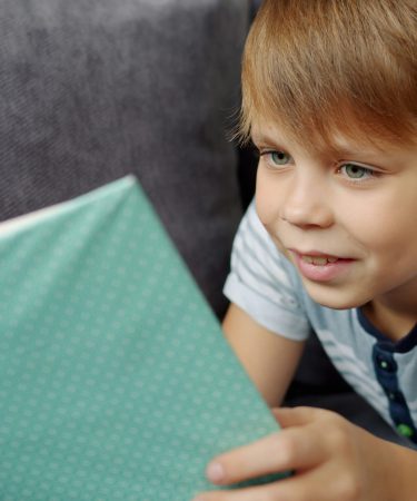 Na zdjęciu widać chłopca leżącego na kanapie, który z zaciekawieniem czyta książkę o zielonej okładce.
